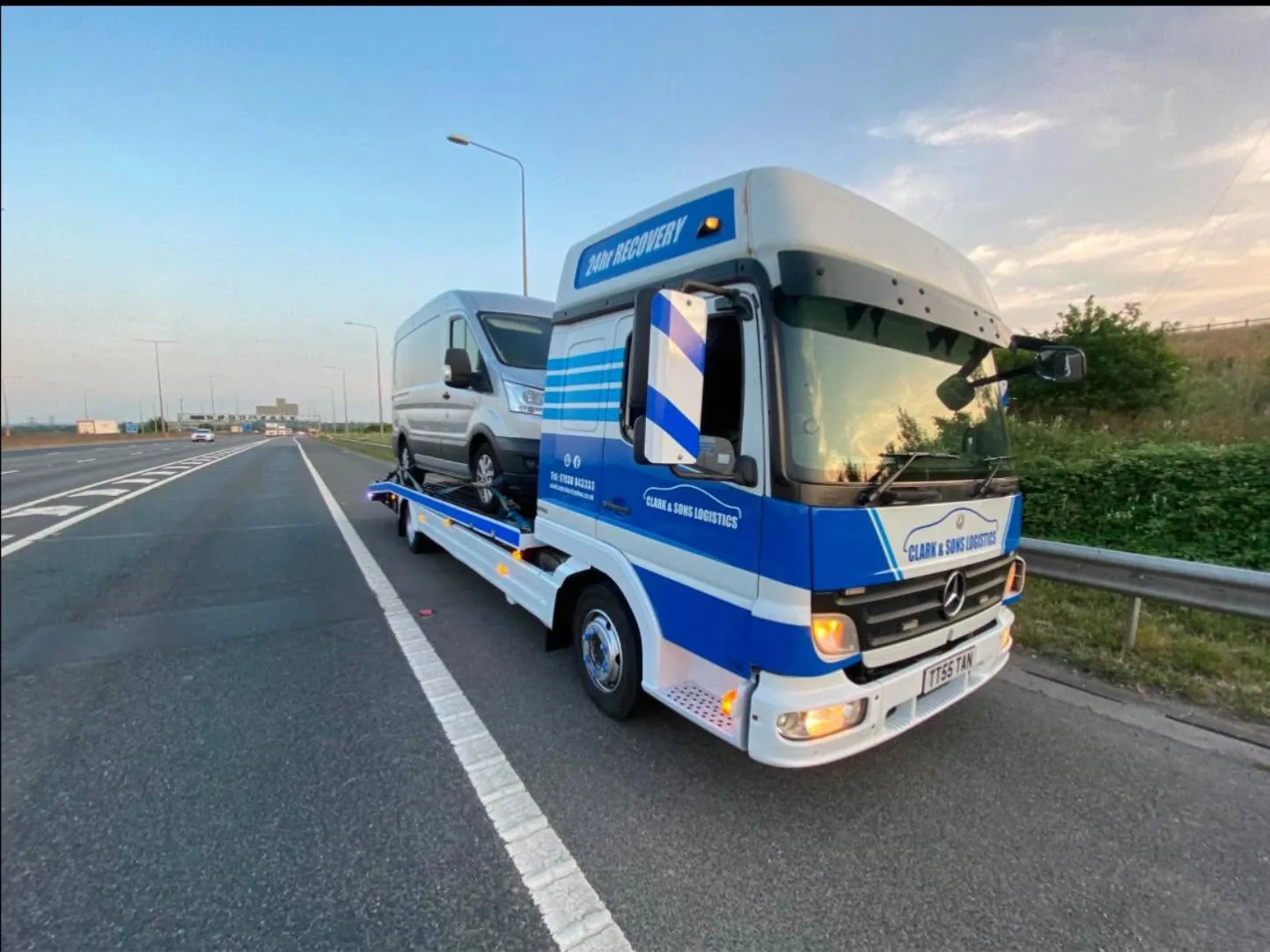 Clark & Sons Logistics recovery truck transporting a silver van on a motorway hard shoulder